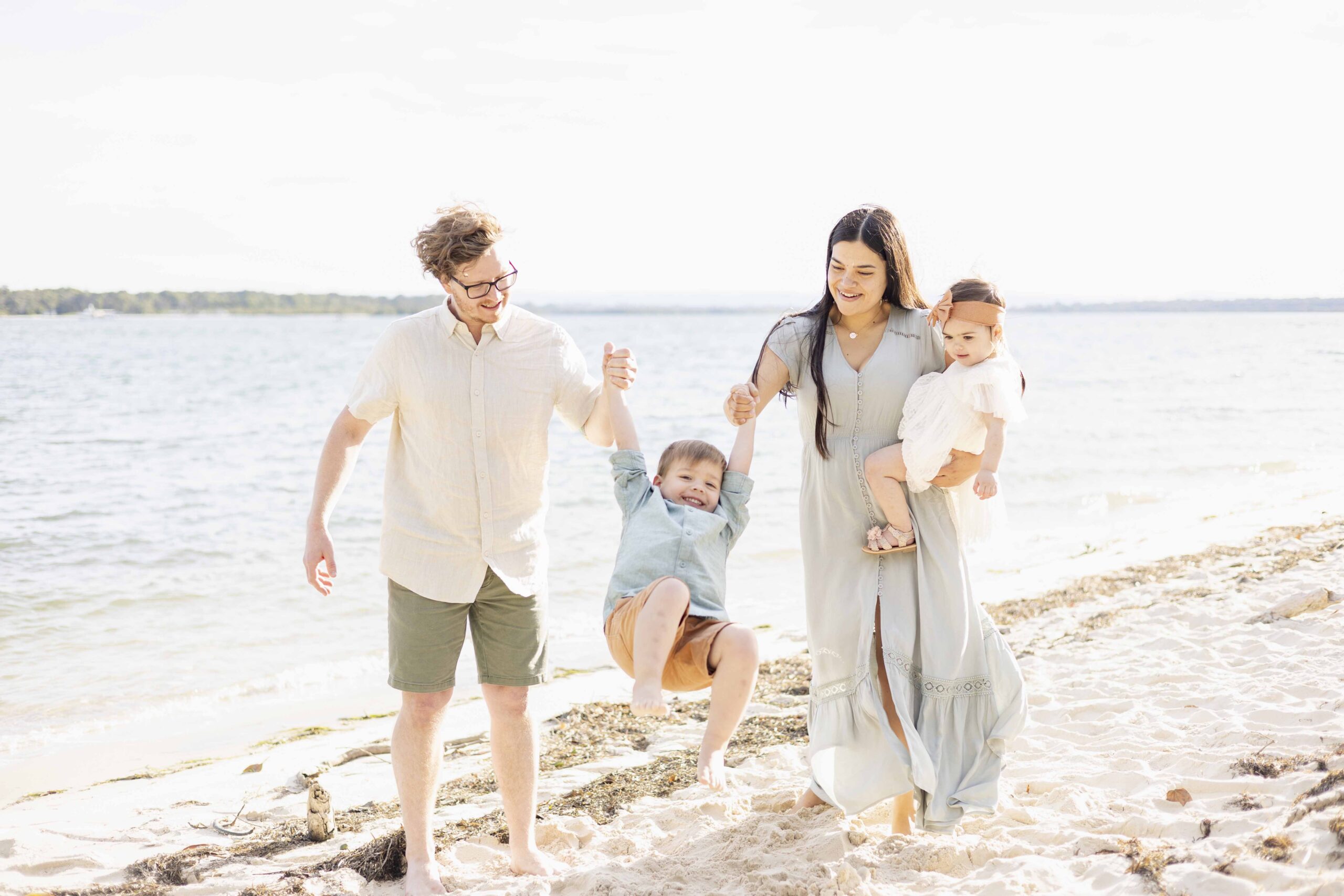 Family of four having fun on the beach. The parents are swinging their little boy. | Bribie Island family photos | Sharon Joseph Photography