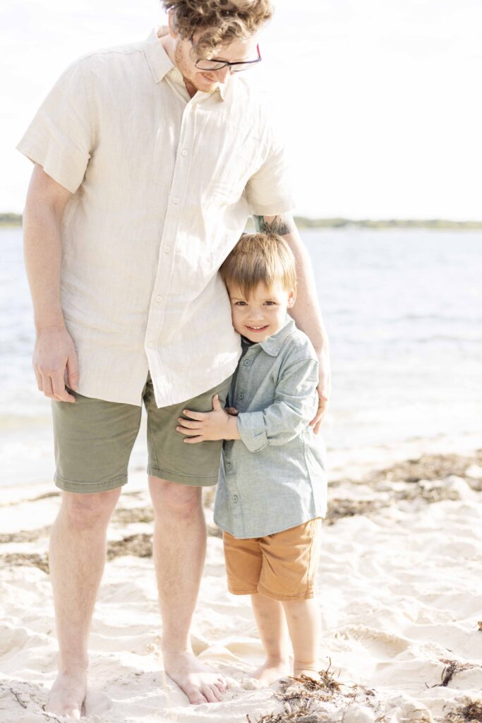 Photo of a young boy wrapping his arms around his daddy's leg. By Sharon Joseph Photography, Brisbane Family Photographer.