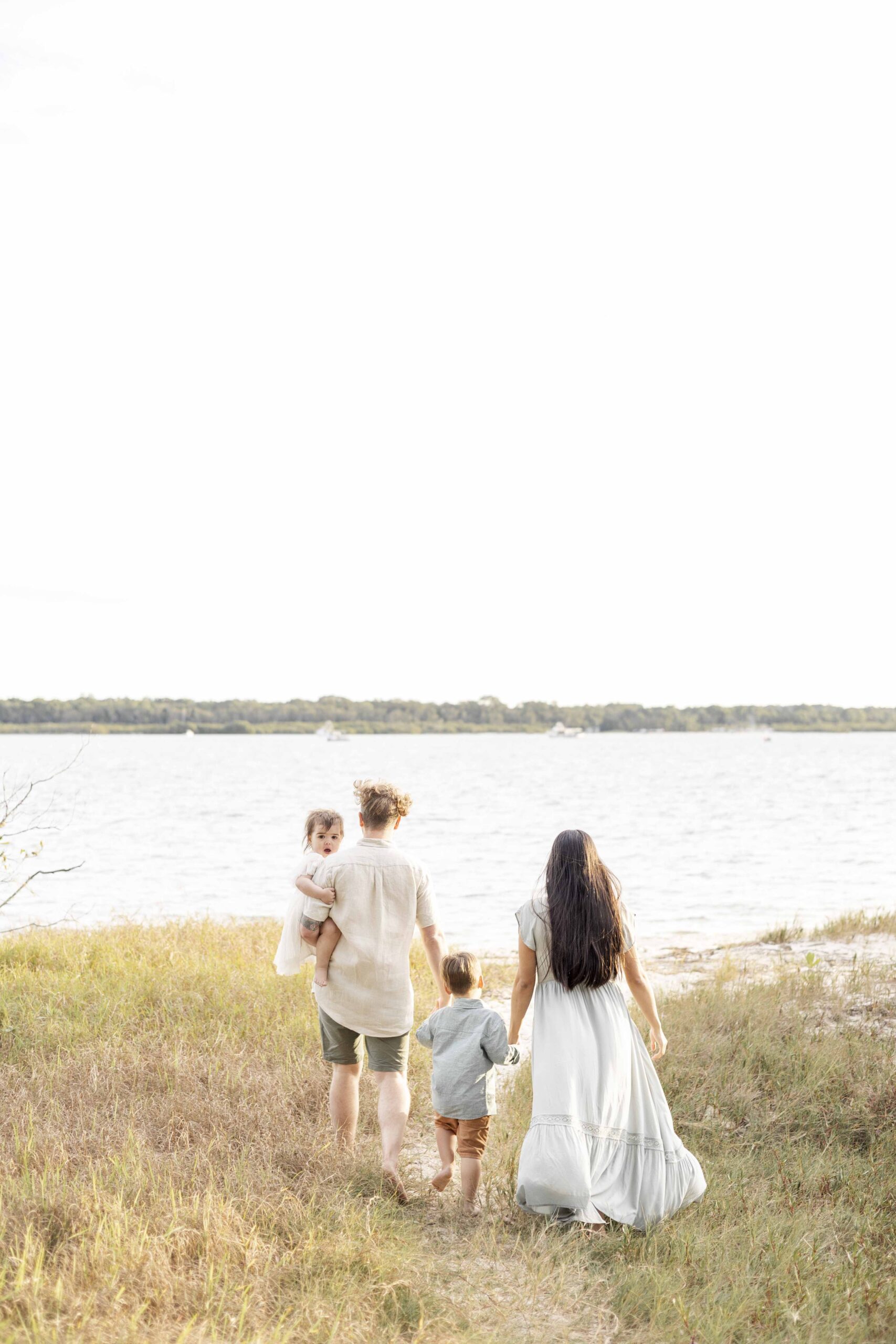 Family photo of mum, dad and two little kids walking towards beach. By Sharon Joseph Photography, Brisbane Family Photographer