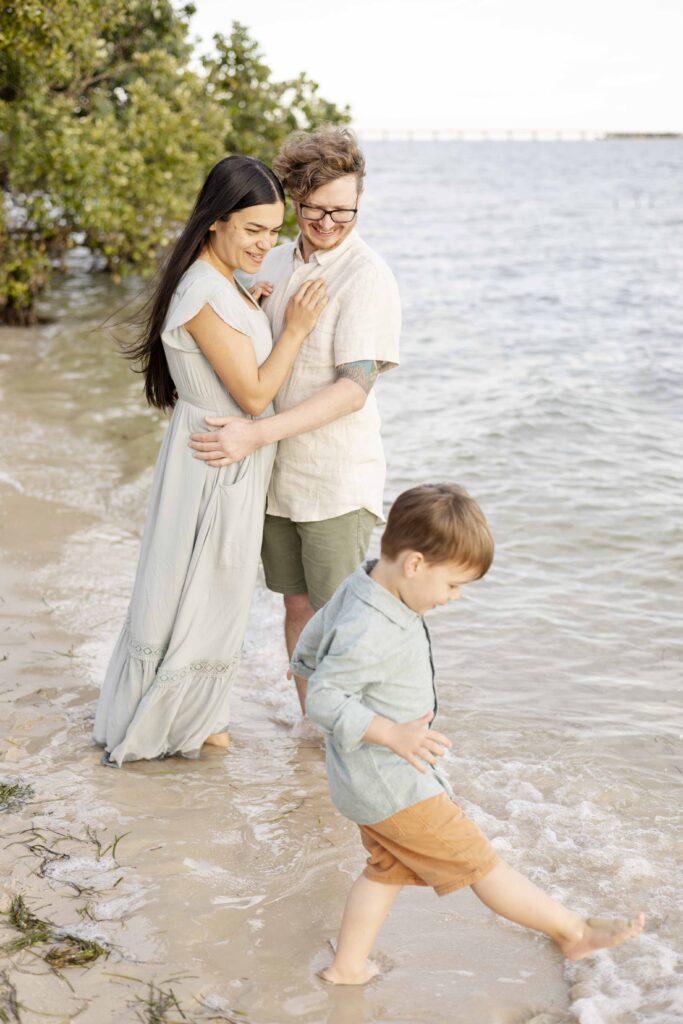 North Brisbane Family Photography | Parents warmly smile at their little boy playing by the water's edge | By Sharon Joseph Photography