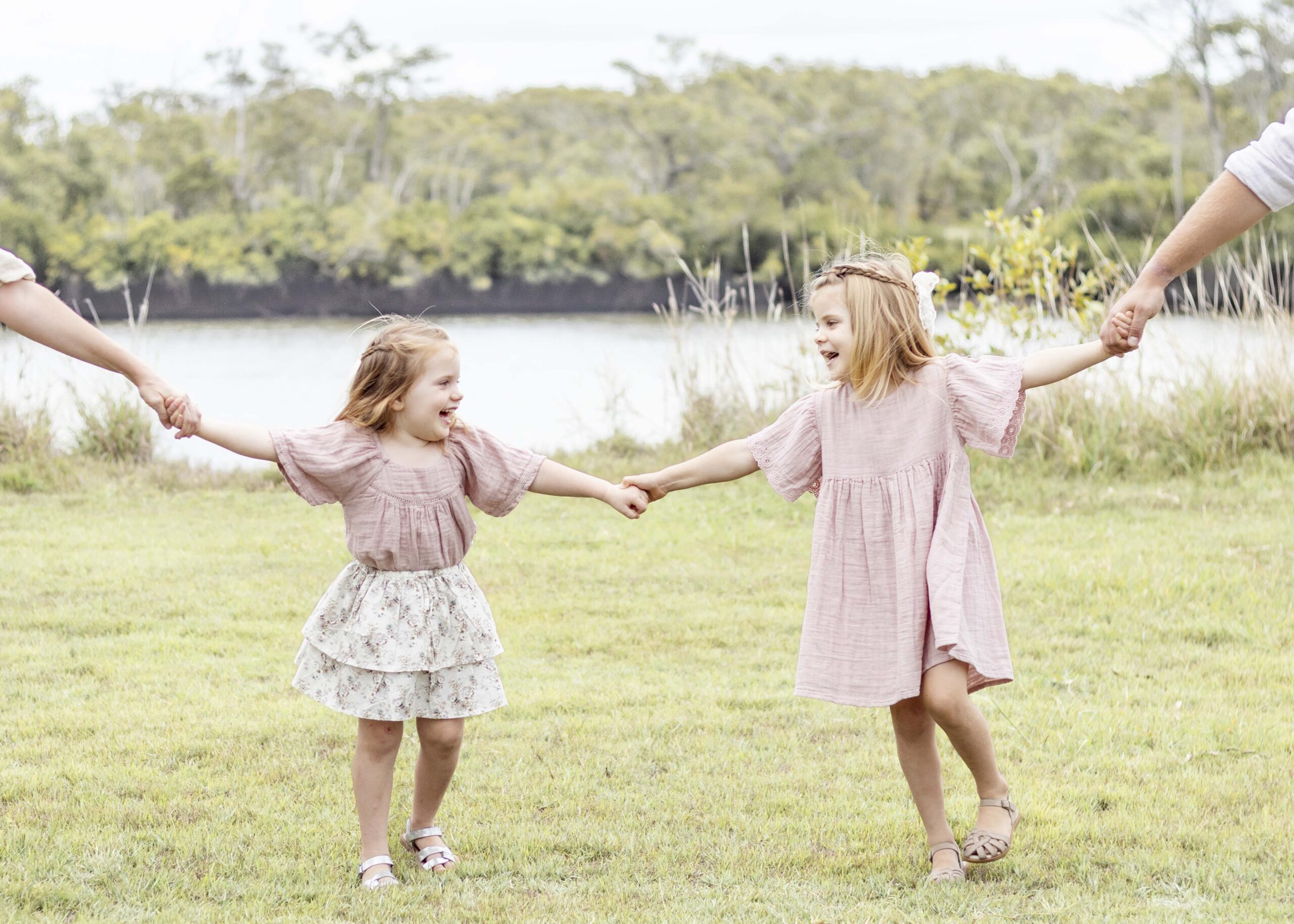 Two sisters joyfully smiling while holding hands. Brisbane Family Photography by Sharon Joseph