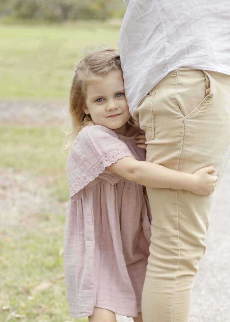 Little girl wrapping her arms around her dad's leg. Brisbane Family Photography by Sharon Joseph.