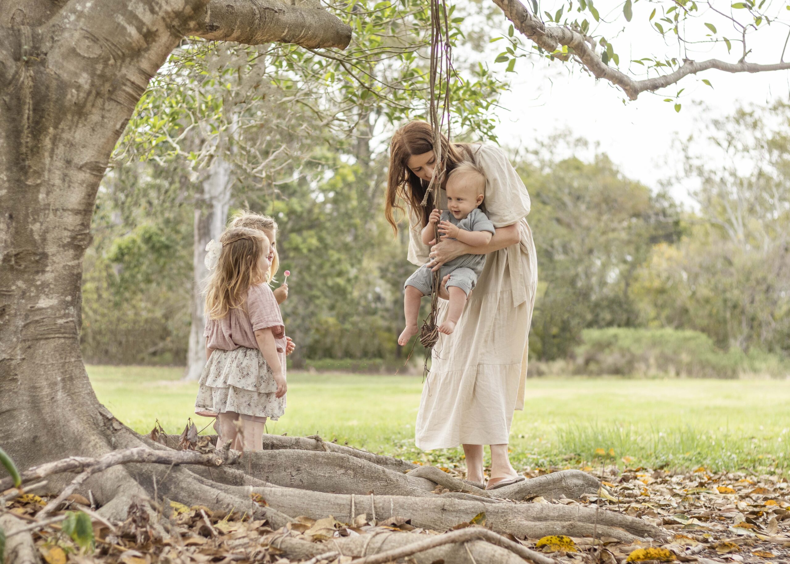 Mum helps little boy hold a rope swing as his two older sisters watch on. Brisbane Family Photography by Sharon Joseph