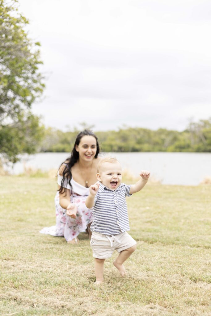 A happy toddler walks as his mum smiles on