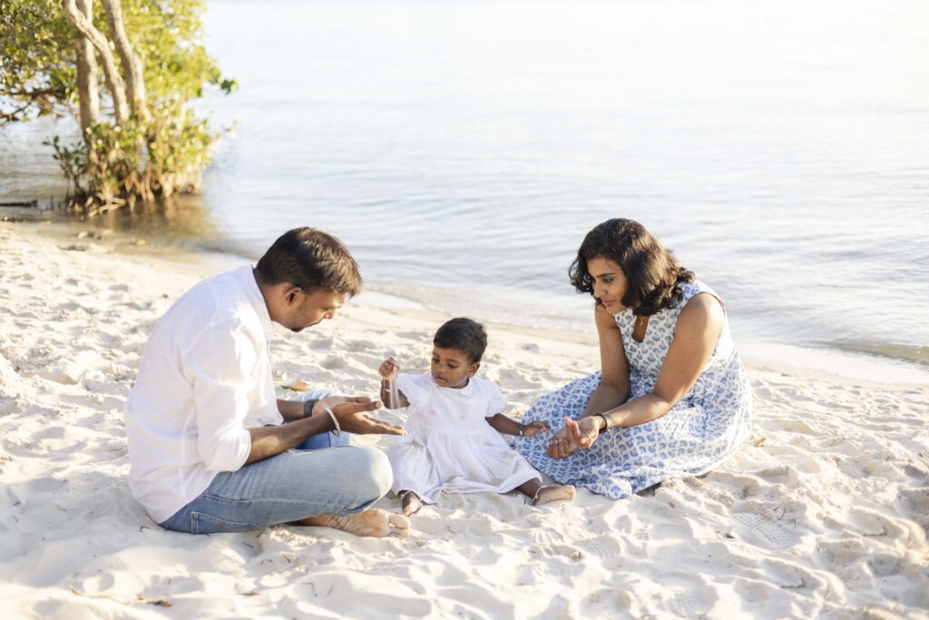 A baby girl playing with sand by the seashore with her parents