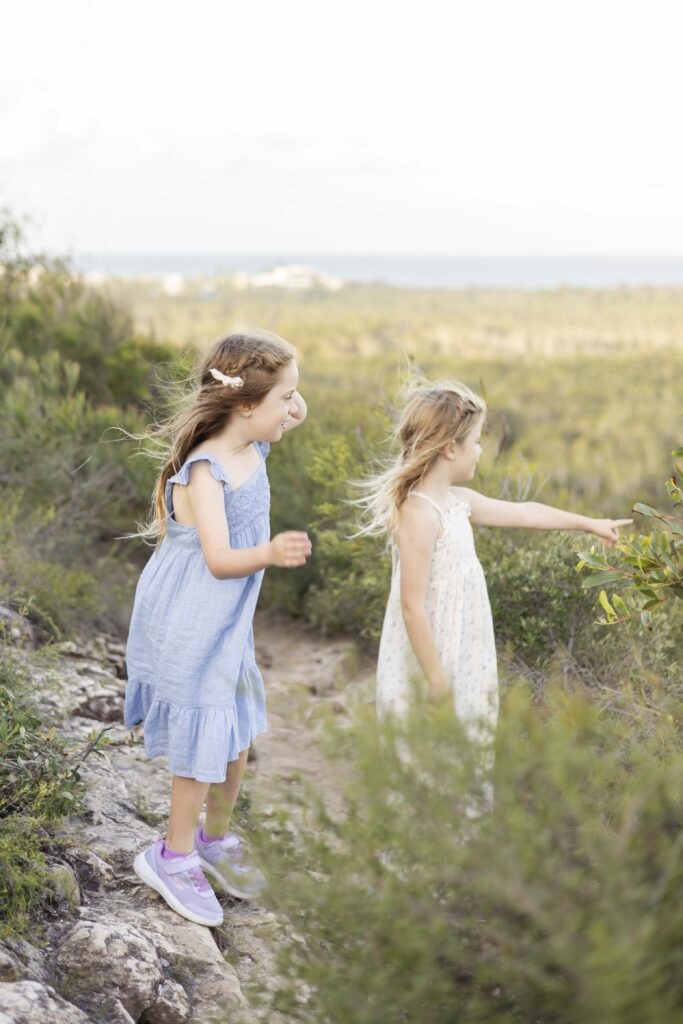Big sister showing little sister a cool plant leaf during their kid friendly bushwalk on Emu Mountain, during a family photoshoot by Sharon Joseph Photography