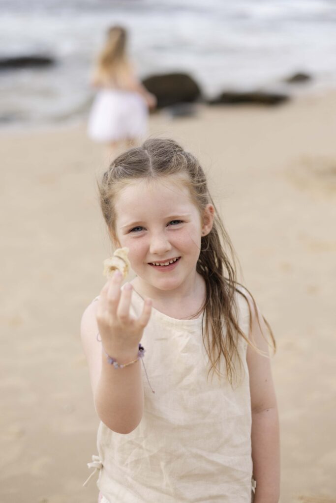 Little girl holding up a shell she found on the beach, during their family photoshoot at Point Cartwright on Sunshine Coast
