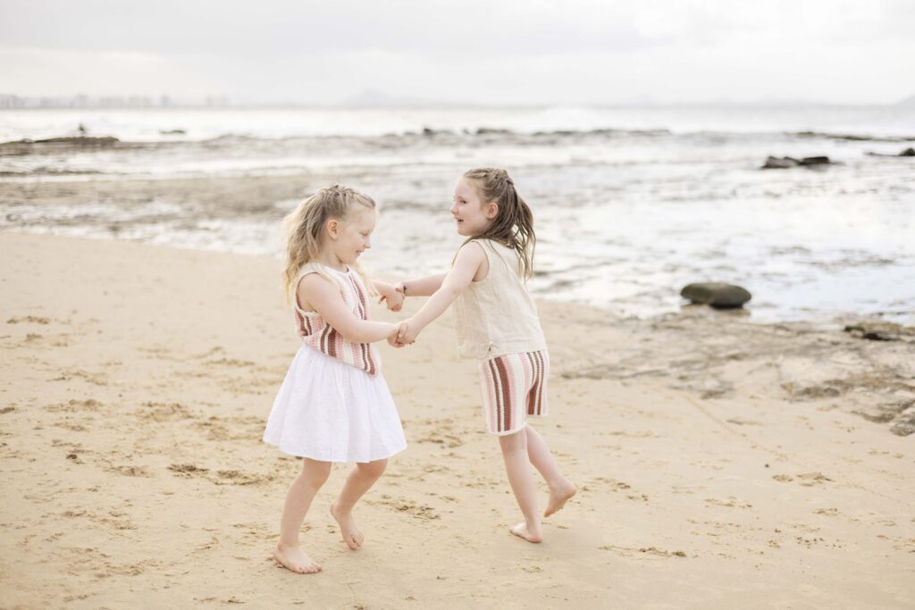 Two girls playing ring-around -the rosie at their family photo session on the beach