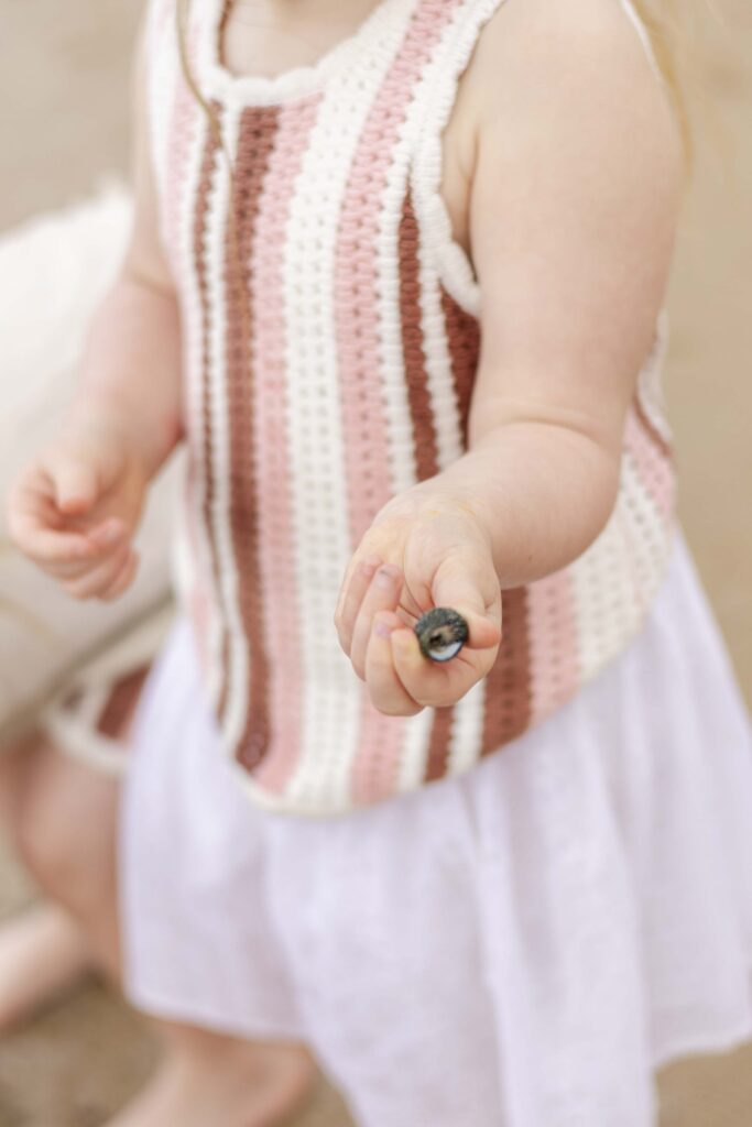 Little girl holding up a shell she found on the beach, during their family photoshoot at Point Cartwright on Sunshine Coast
