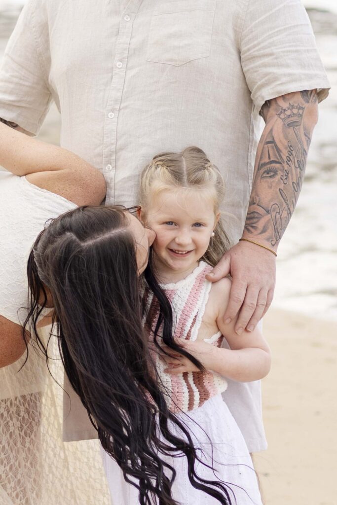 mum kissing daughter's cheek at their family photoshoot at Point Cartwright on Sunshine Coast