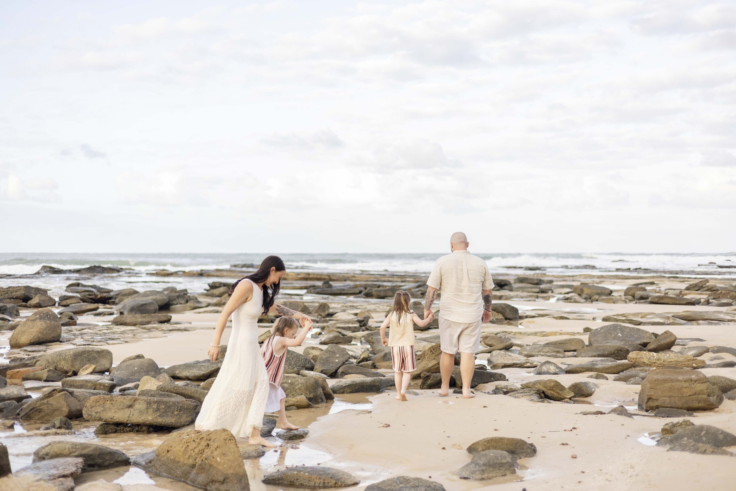 Family of four walking along a rocky beach at Point Cartwright during their family photoshoot