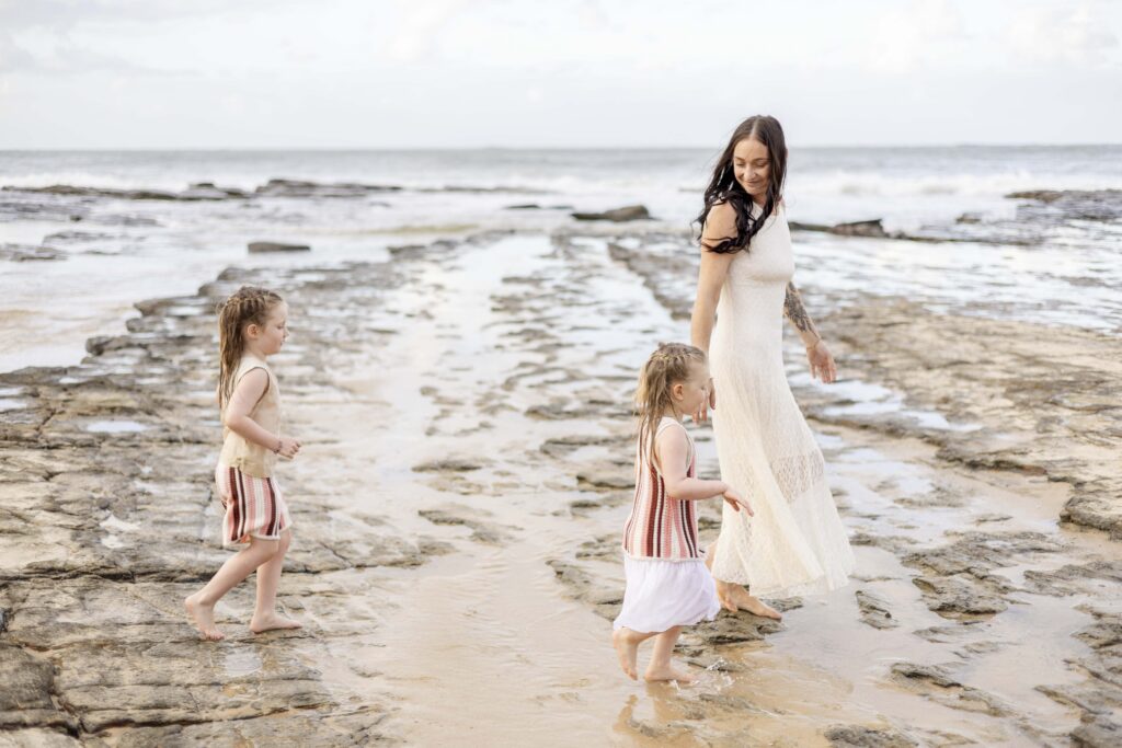 Mum and daughters walking along Point Cartwright Beach, with mirror-like water