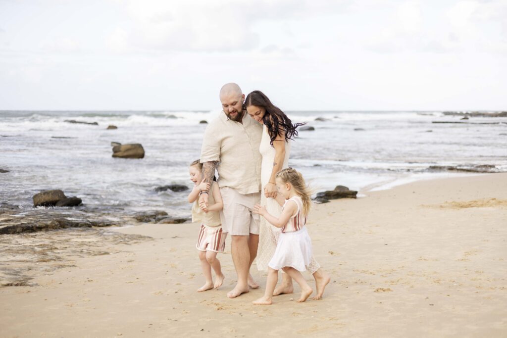 Family of four embracing each other by the beach, during their family photoshoot at Point Cartwright on Sunshine Coast