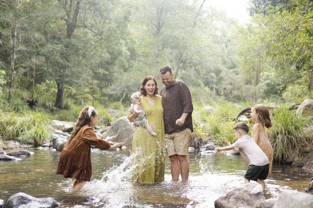 Family having fun at this kid-friendly creek near Brisbane. They are wearing well coordinated family outfits win earthy greens and warm browns, complementing the hues of their leafy, creek backdrop.