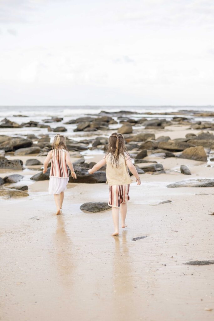 Two girls walk towards the water on a rocky beach at Point Cartwright, photo by Sharon Joseph, Brisbane Family Photographer. It is totally okay if kids don't cooperate for family photos.