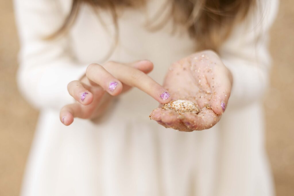 Girl with sparkly pink nailpolish exploring a seashell at a beach family photoshoot in Brisbane.