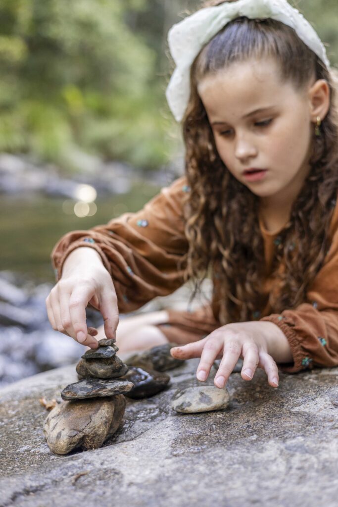 Girl building a rock tower at Cedar Creek in Samford. Natural, Documentary Brisbane Family Photography.